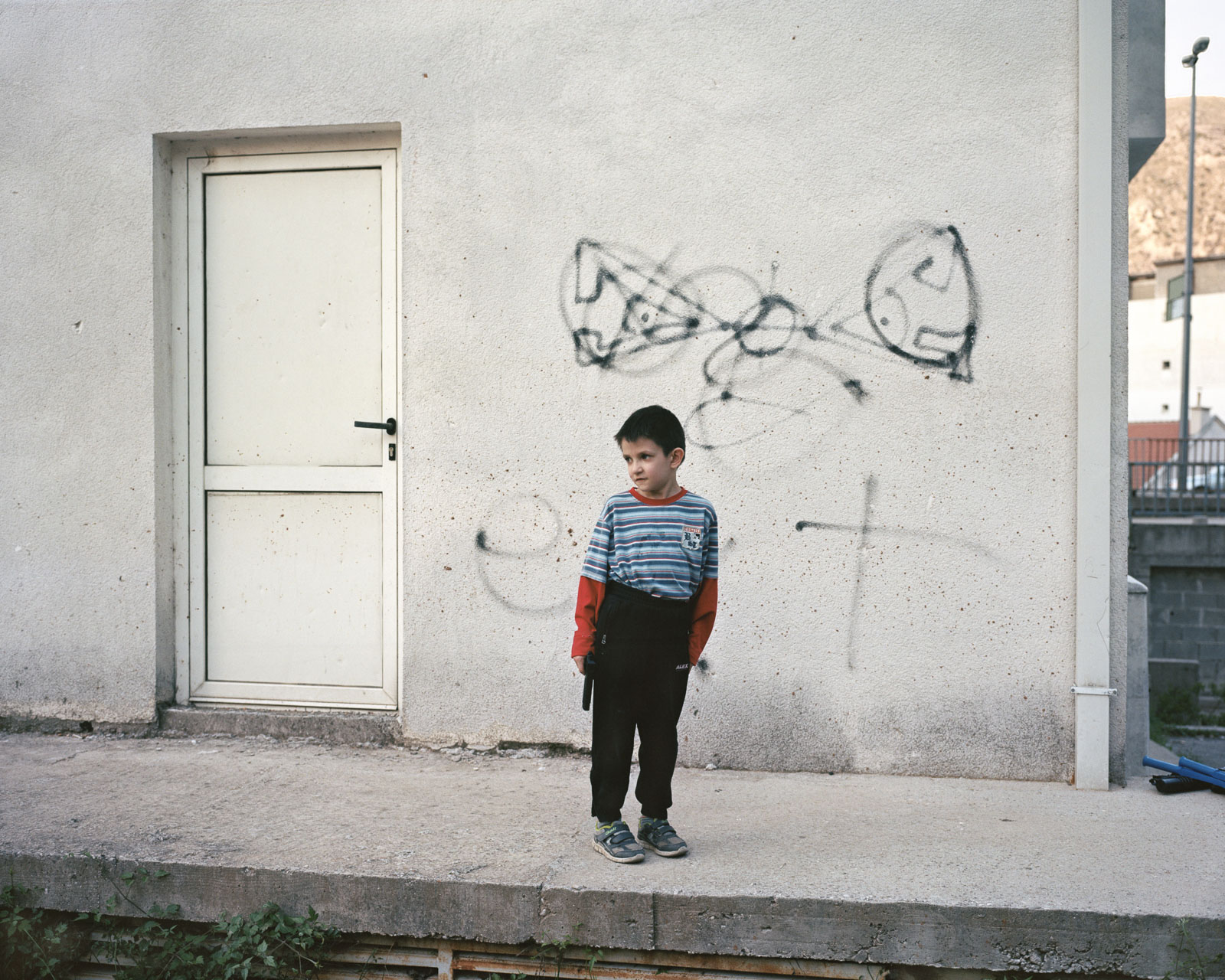 Ein Junge in Mostar mit einer Spielzeugpistole in einer Hand und einem religiösen Symbol an der Wand hinter ihm